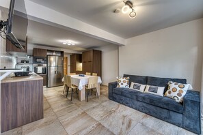 A compact kitchen with modern appliances, a dining area with a table and chairs, and a dark-colored sofa with patterned cushions. - Ti'Bulle - Petfriendly - Jacuzzi (Saint-Pierre)