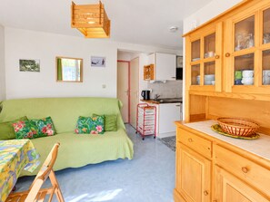 Un salon chaleureux avec un canapé vert, un meuble en bois doté de portes en verre et, au fond, une cuisine.