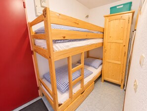 Un lit superposé avec une structure en bois, une petite armoire et une porte rouge.