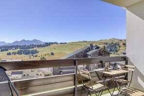 A balcony with a view of a mountainous landscape, a wooden table with chairs, and a building with a sloped roof. - Plein Soleil - Balcon - Proche pistes (Hauteluce)