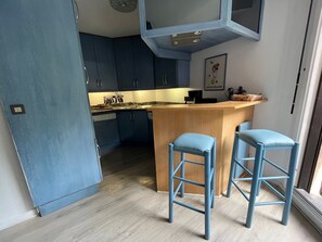 A modern kitchen with dark blue cabinets, a wooden island with stools, and a painting on the wall. - Family duplex, pets welcome, parking - 6 guests (Brides-les-Bains)