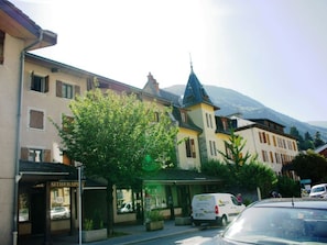 A street view with a row of buildings, including a hotel with a sign that reads "HOTEL". There is a tree in the foreground, and a van is parked on the street. - Family duplex, pets welcome, parking - 6 guests (Brides-les-Bains)