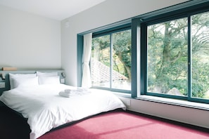 Un dormitorio con una ventana grande, una cama y una mesita de noche.