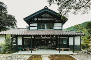 Un edificio japonés tradicional con techo de tejas, entrada cubierta y un pequeño jardín con bancos.