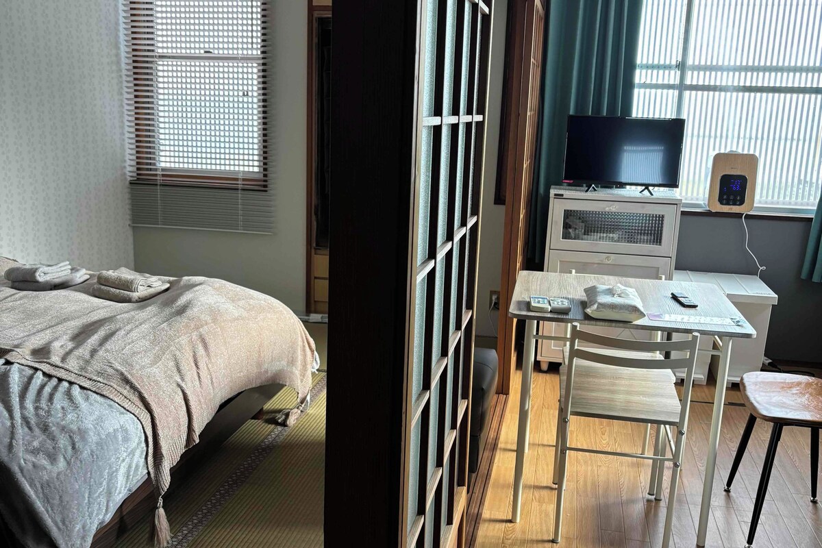 A room with a bed, a desk, a TV, and a window with blinds.