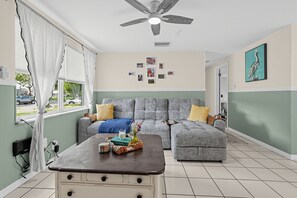 Una sala de estar con un sofá gris, una mesa de centro, un ventilador de techo y una pared con cuadros enmarcados.