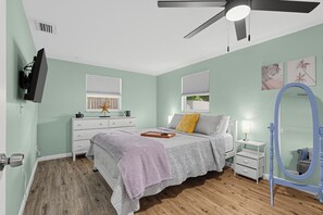 Un dormitorio con cama, mesitas de noche, cómoda, ventilador de techo y televisor montado en la pared.