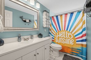 Un baño con un lavamanos blanco, un espejo, un inodoro y una cortina de ducha con diseño de sol.