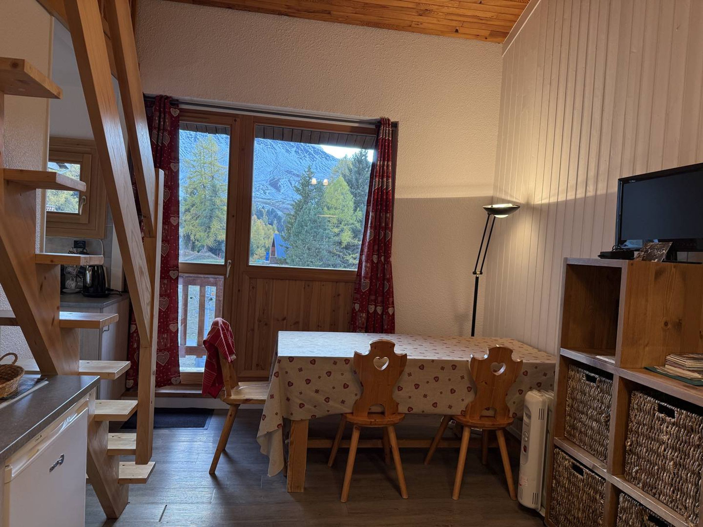 A cozy room with a wooden table and chairs, a television, and a view of trees through a window.