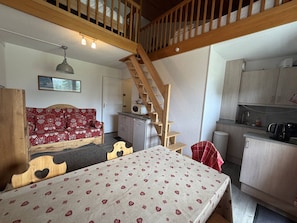 A cozy room with a bed, a wooden staircase, a kitchenette, and a red patterned sofa. - Duplex apartment with mountain view - 6 guests (Plagne Villages)