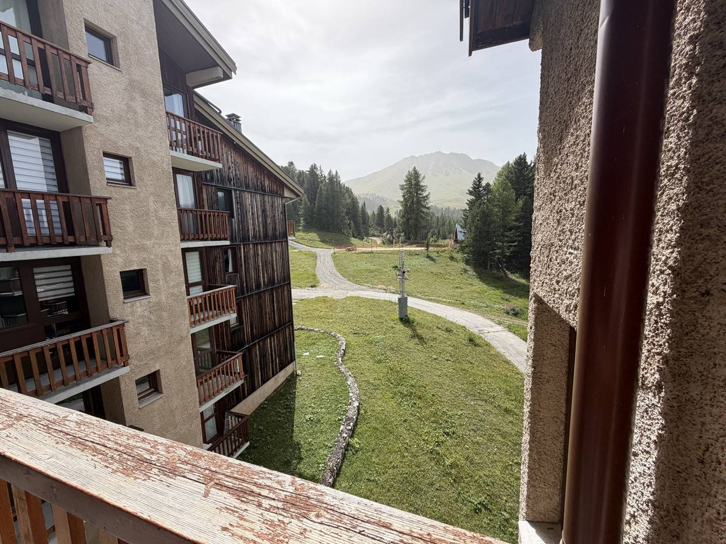 Un edificio de varios pisos con balcones, un área verde y una montaña al fondo.