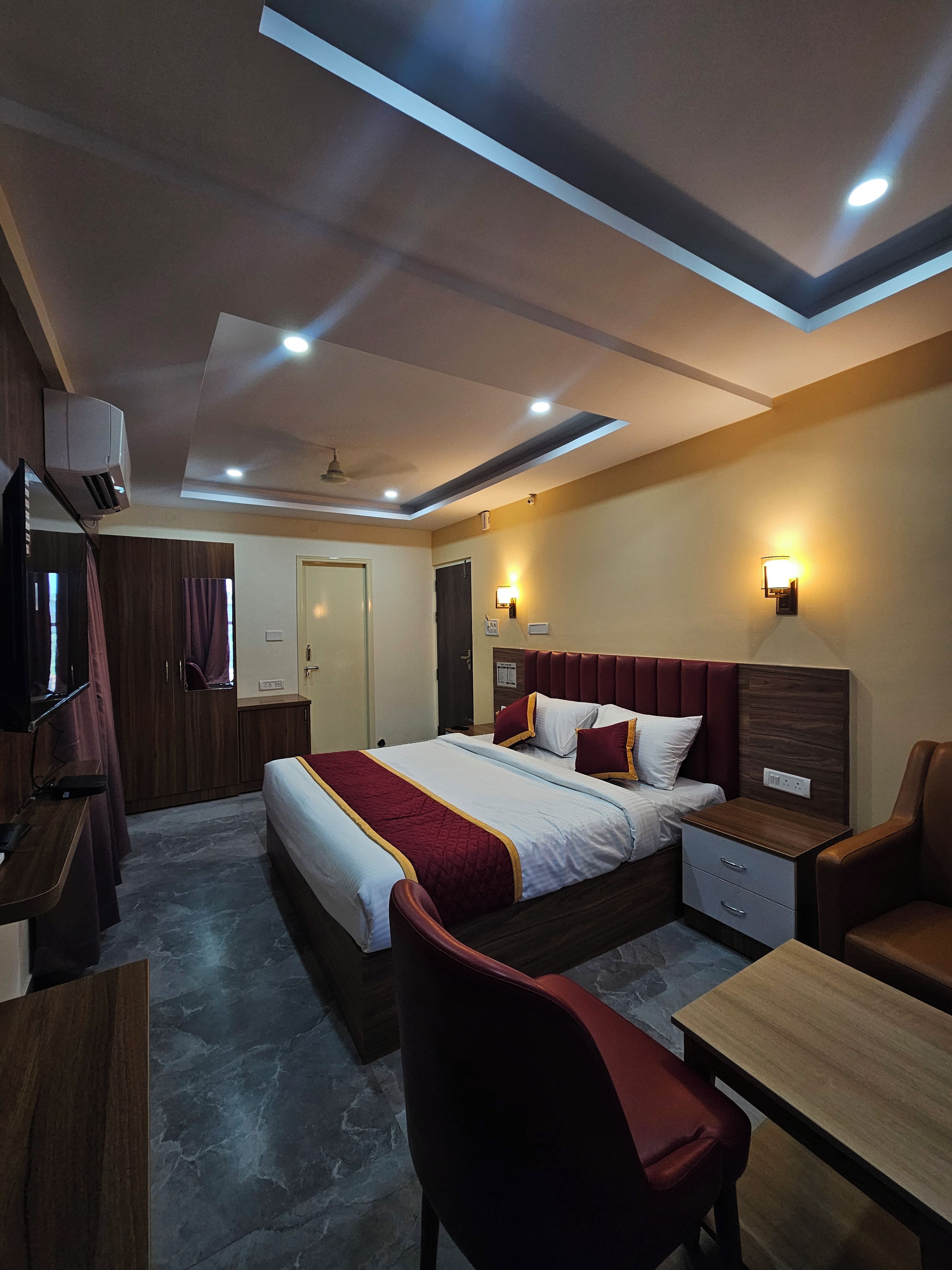 A hotel room with a bed, bedside tables, a desk, a chair, and a television.