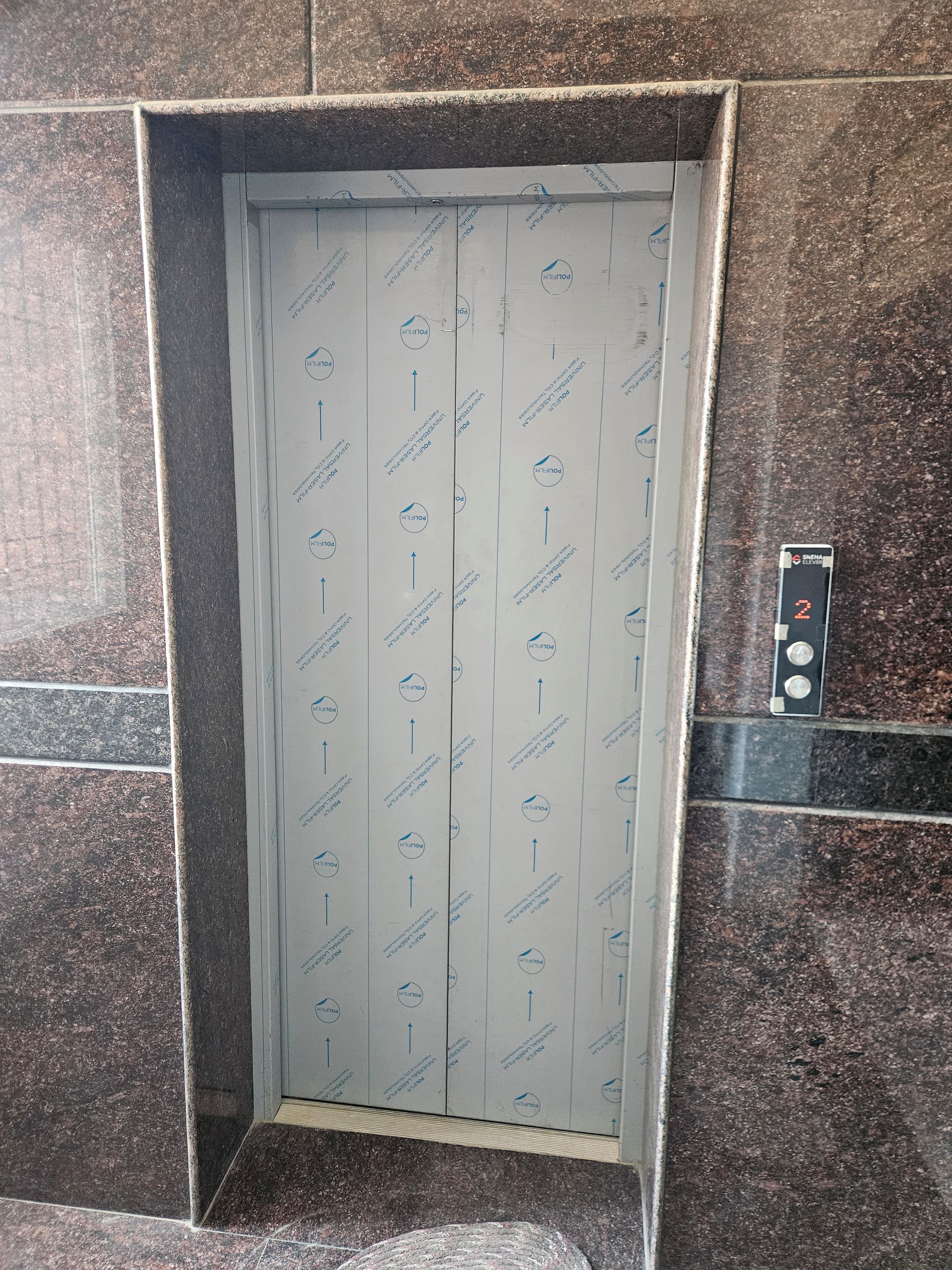 Un ascensor con una pared con diseño y un panel de control con un botón marcado '2'.