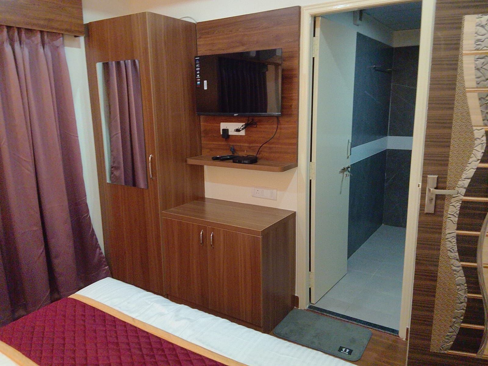 Un dormitorio con una cama, un armario de madera, un televisor y una puerta que da a un baño.