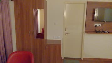 Una habitación con un armario de madera, una silla roja, un televisor montado en la pared y una puerta con un felpudo en el suelo.