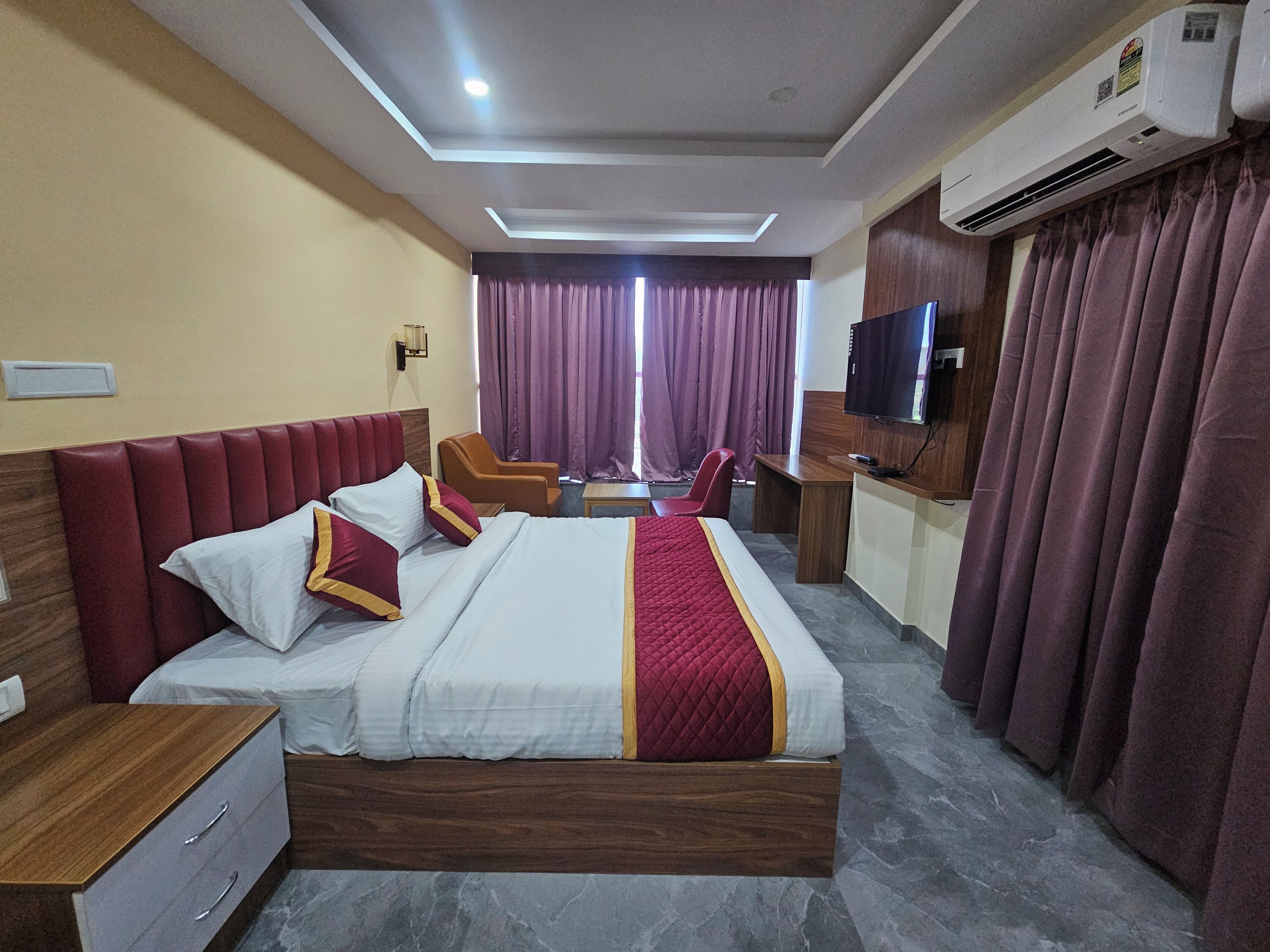 A hotel room with a bed, a desk, a chair, a TV, and an air conditioning unit.