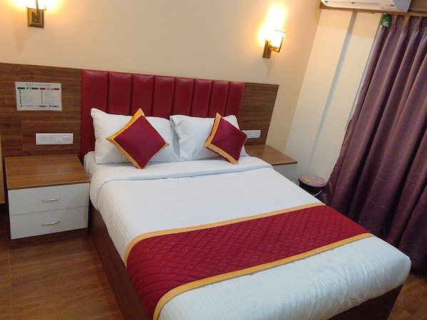 A hotel room with a bed, nightstands, a red headboard, a white bedspread, and a red and white quilted blanket. - Regal Suites Hotel Rooms Bommasandra (Bommasandra ,Bangalore)