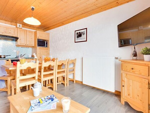 A kitchen with wooden cabinets, a dining table with chairs, a microwave, and a radiator. - Spacious apartment by the slopes - 8 guests (Les Menuires)