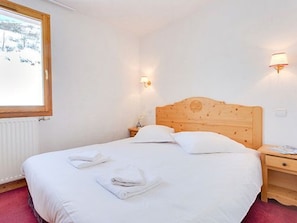 A hotel room with a wooden headboard, a bed with white linens, two bedside tables, and a window with a view of trees. - Spacious apartment by the slopes - 8 guests (Les Menuires)