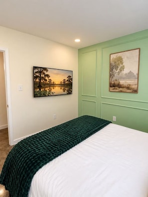 Un dormitorio con cama, dos cuadros en las paredes y una pared de acento verde.