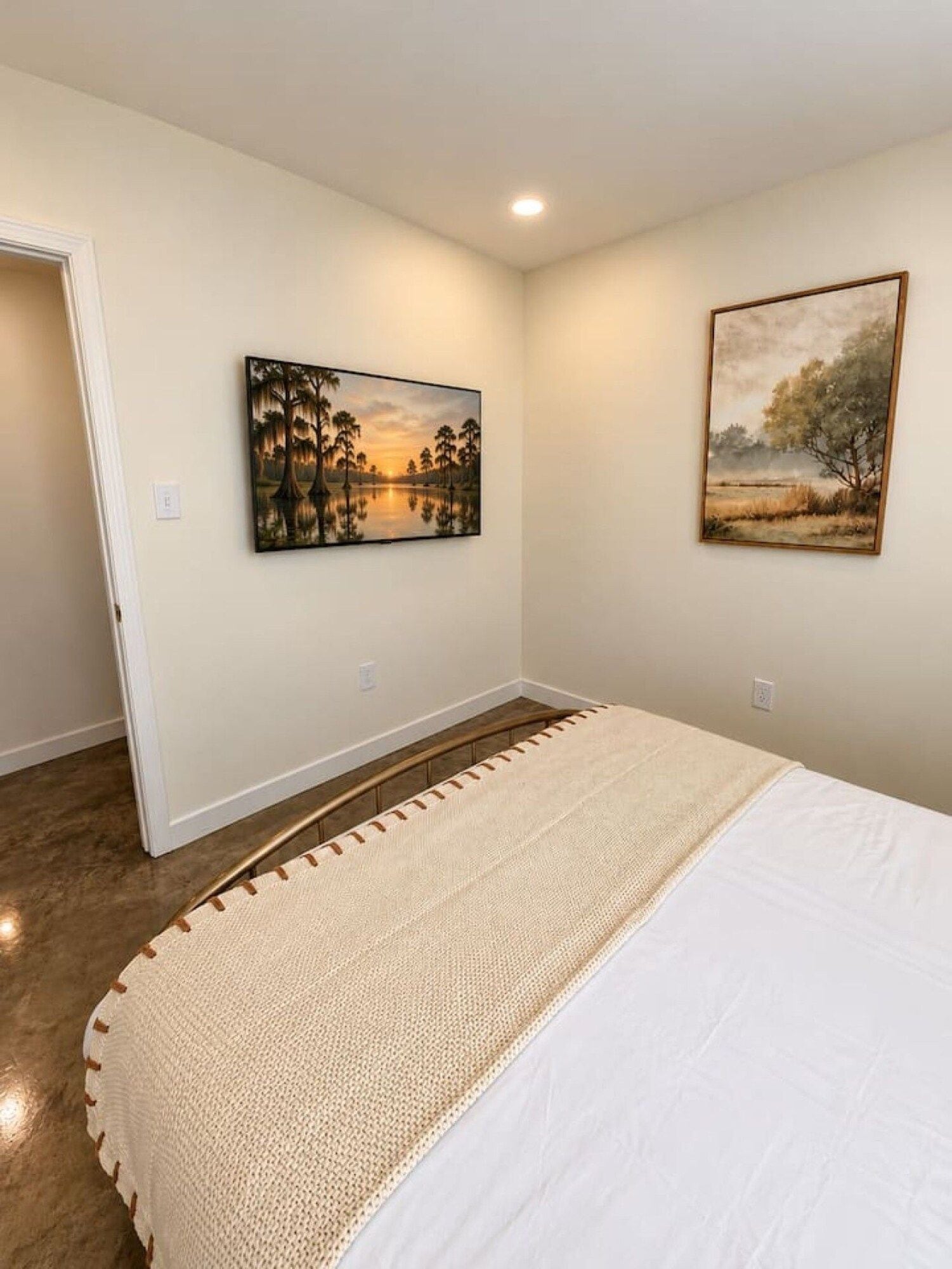 Un dormitorio con una cama, dos cuadros en la pared y una puerta que da a otra habitación.