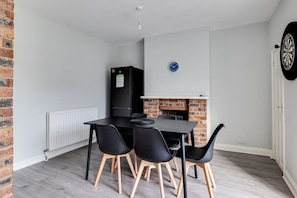 A dining area with a black table and chairs, a black refrigerator, a clock, and a dartboard. - Bright 3-bed Home Crewe Garden Netflix Wi-fi (Crewe)