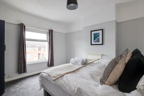 A hotel room with a bed, a window with curtains, a framed picture on the wall, and a radiator. - Bright 3-bed Home Crewe Garden Netflix Wi-fi (Crewe)