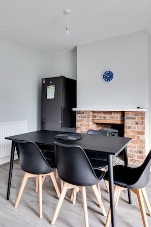 Een moderne keuken met een zwarte koelkast, een schouw met bakstenen en een eettafel met vier stoelen.