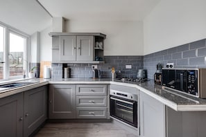 Een moderne keuken met grijze kastjes, een ingebouwde oven, een magnetron en een gasfornuis.