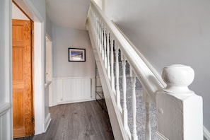 A hallway with a wooden door, a white railing, and a framed picture on the wall. - Bright 3-bed Home Crewe Garden Netflix Wi-fi (Crewe)