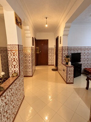 A hallway with patterned walls, a wooden door, a television, and a small table with a vase. - Moroccan Home • Central Tangier + Free Parking (Tanger)