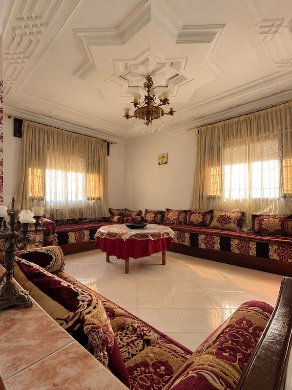 A room with a large, ornate sofa set, a round table, and a chandelier.