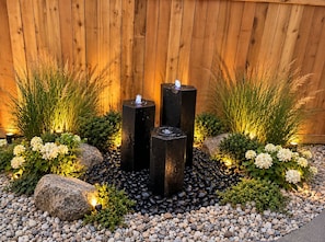 A garden with three black stone pillars, surrounded by pebbles, white flowers, and tall grasses. - Spacious 4BD home with hot tub, game room, fully fenced large corner lot. (Monroe)