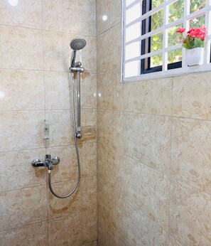 Eine Dusche mit Duschbrause und Wandarmatur, vor einer gefliesten Wand.