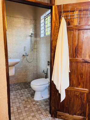 Ein Badezimmer mit Toilette, Waschbecken, Dusche und einer Holztür.