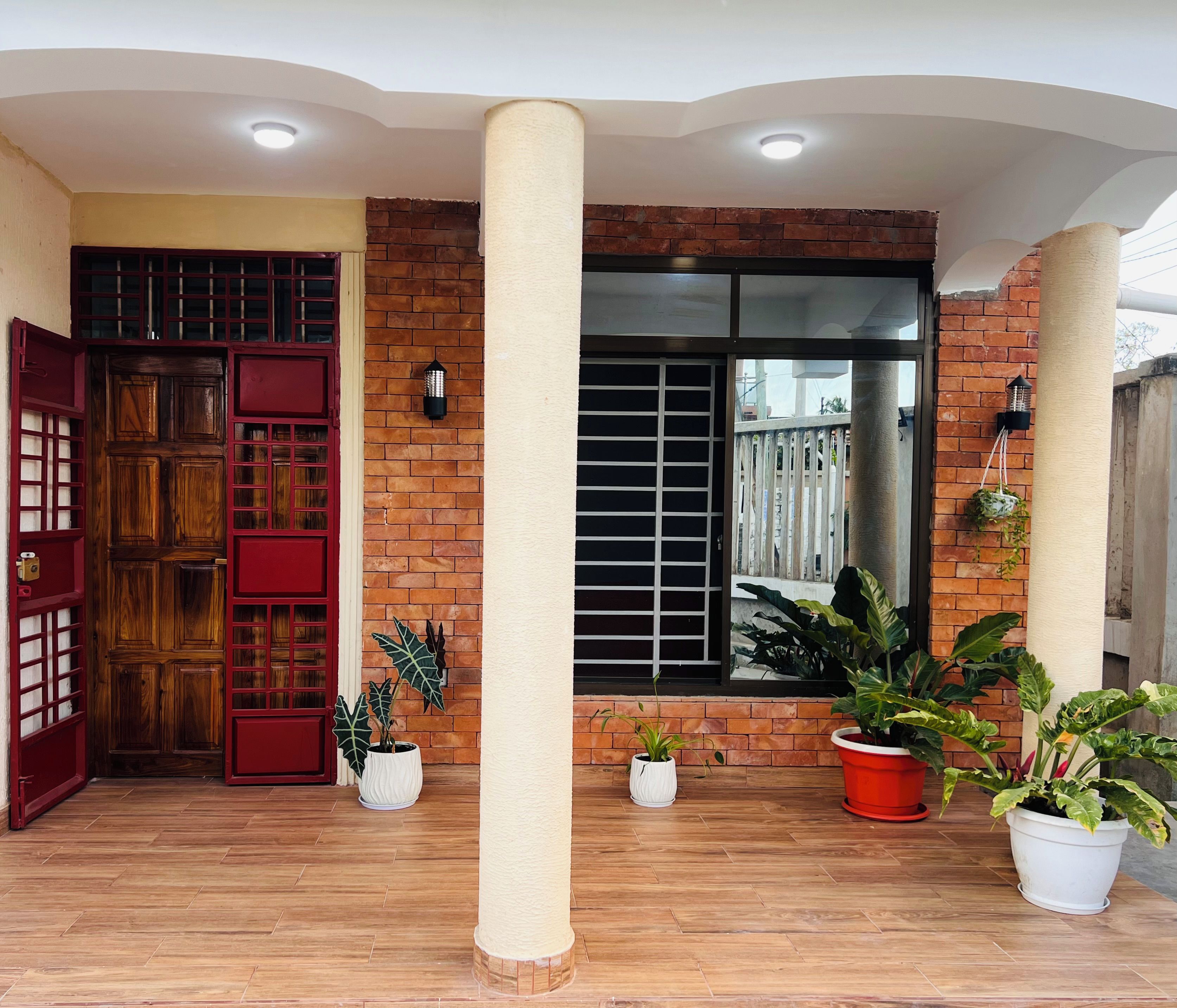 A covered porch with a wooden door, brick walls, and potted plants.