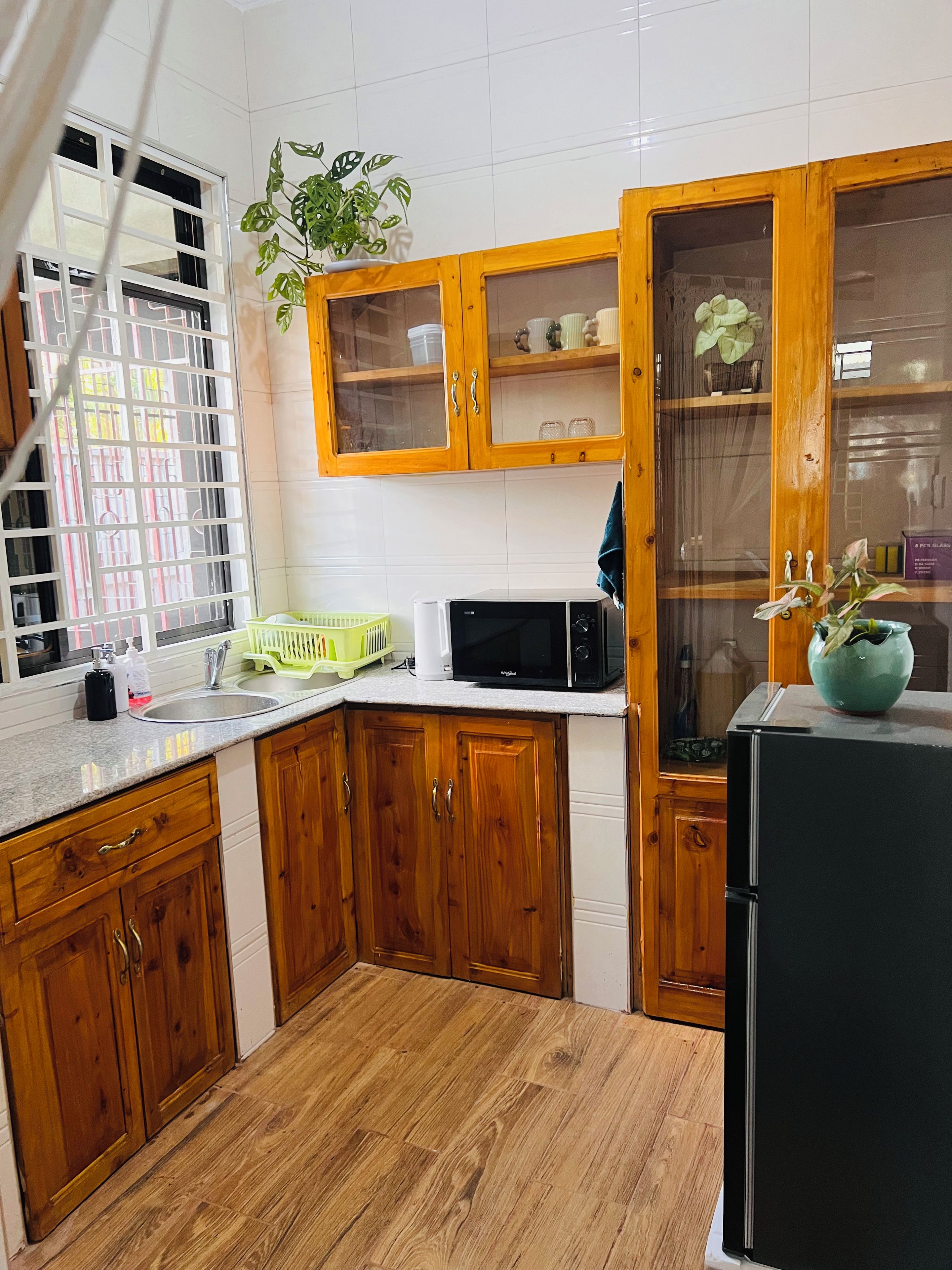 A kitchen with wooden cabinets, a microwave, a refrigerator, and a window with a view.