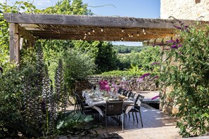 An outdoor dining area with a pergola, stone wall, and lush greenery. - New Listing (Milhac-de-Nontron)