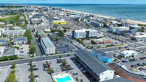 A coastal cityscape with a prominent hotel featuring a swimming pool and a parking lot. - Bayside 1BR Condo with Pool (Ocean City)