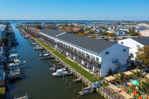 A marina with docked boats, a long building with a covered walkway, and a residential area in the background. - Bayside 1BR Condo with Pool (Ocean City)