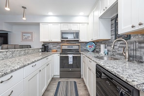 A modern kitchen with white cabinets, a built-in microwave, a stainless steel oven, and a granite countertop. - Bayside 1BR Condo with Pool (Ocean City)