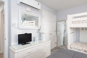 A bedroom with a bunk bed, a television, a dresser, a mirror, and a door leading to another room. - Bayside 1BR Condo with Pool (Ocean City)