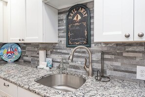 A kitchen with a granite countertop, a stainless steel sink, and a chalkboard with 'Sail Away' written on it. - Bayside 1BR Condo with Pool (Ocean City)