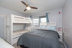 A bunk bed room with a ceiling fan, a window with curtains, and a bed with a grey quilt. - Bayside 1BR Condo with Pool (Ocean City)