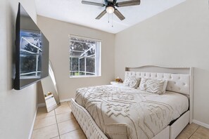 Ein Schlafzimmer mit einem Bett, einem Deckenventilator, einem Fenster und einem flachbildfernseher an der Wand.