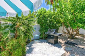Eine Terrasse mit Grill, blauem Stuhl und einer Palme.