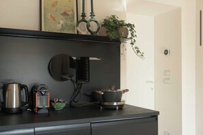 A kitchen with a black countertop, a kettle, a coffee maker, a pot, and a small plant on a shelf. - New Listing (Roma)