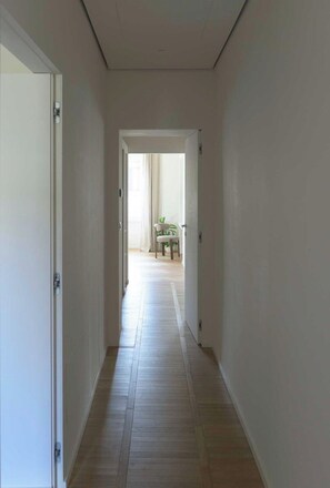 Un corridoio con pavimento in legno che conduce a una stanza con una sedia e un tavolo.