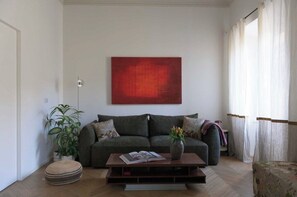 A living room with a sofa, a coffee table, a potted plant, and a red abstract painting on the wall. - New Listing (Roma)