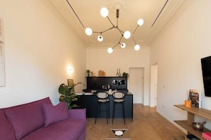 A modern living room with a purple sofa, a kitchen area with a bar, and a dining table with chairs. - New Listing (Roma)